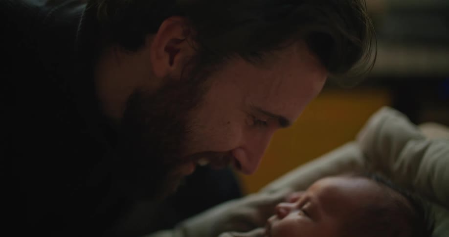 Father touches noses with his newborn baby resting in bed at home