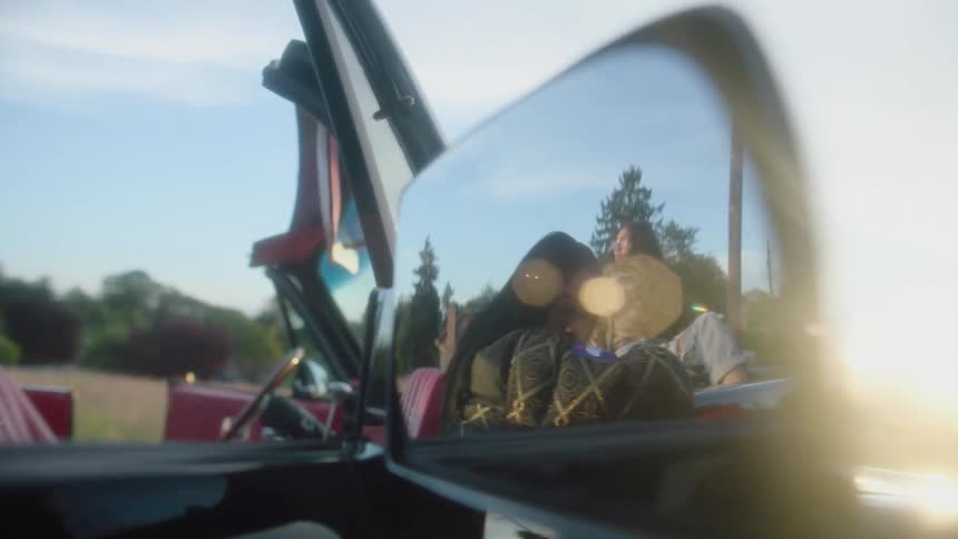 Young models sitting on a convertible car looking at the camera reflecting on the rearview mirror