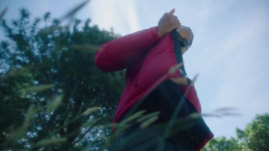 Man standing outdoors examines his jacket under a cloudy sky
