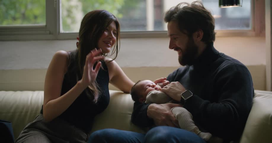 Mom laughs as she talks with her husband who is holding their sleeping baby