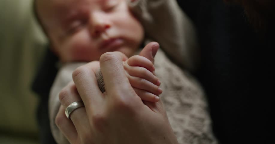 A father holds his newborn son while holding and kissing his tiny hand