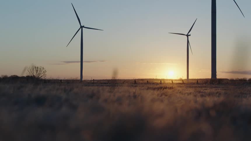 Wind turbines on a wind farm stand tall as the sun shines brightly on the horizon