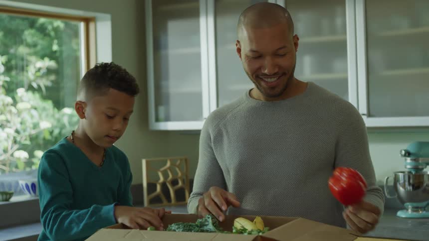 Family unpacking fresh vegetables from a cardboard box in the kitchen at home