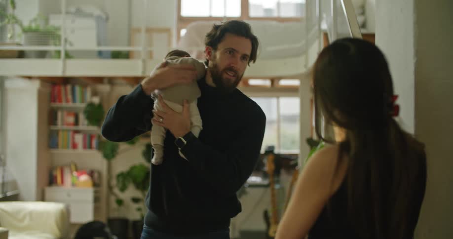 A woman talks with her husband as he holds their baby and rubs his back