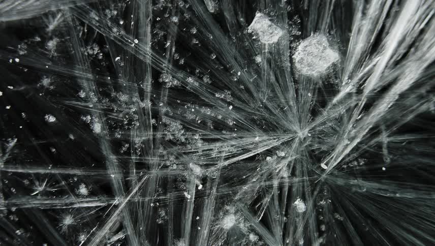 Close up of thin white ice crystals floating and forming against a black background