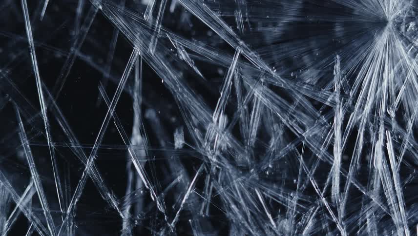 Twisting close up of thing ice crystals forming in front of a black background