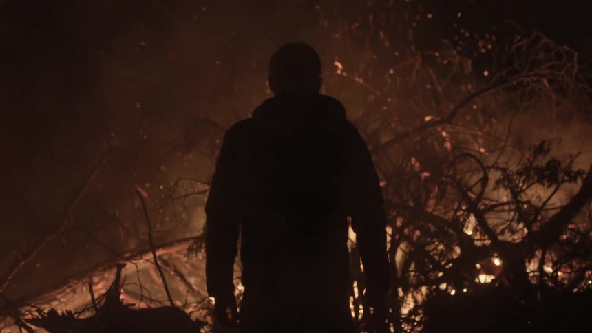 Man watches brush fire in the dark