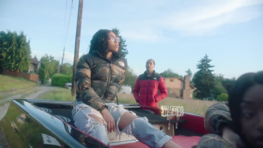 Group of young people standing on and around a convertible car parked in the countryside