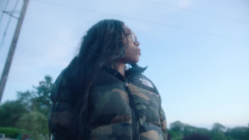 Young woman wearing a thick jacket reclined outdoors under a blue sky