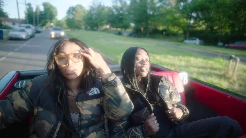 Two young beautiful woman wearing thick jackets sitting on the back seat of a convertible driving in the morning