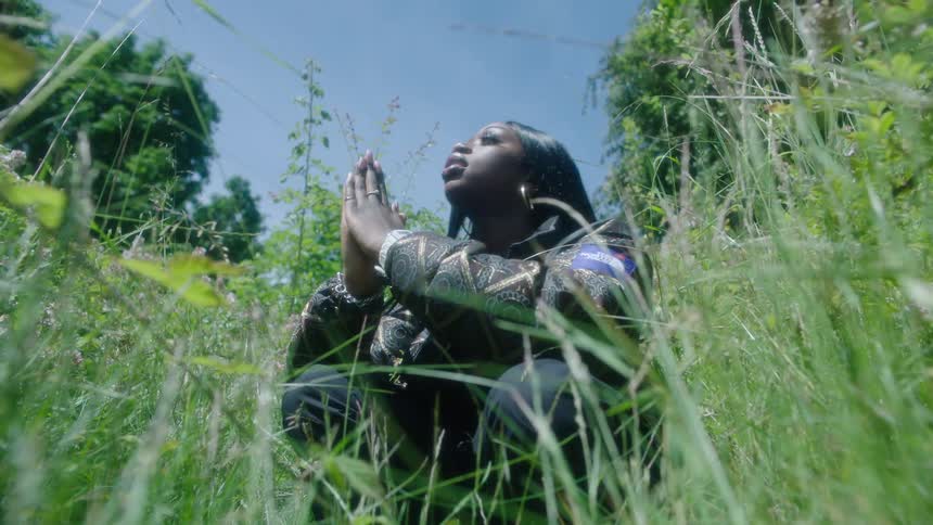A woman sitting in the tall grass swaying to music on a bright day