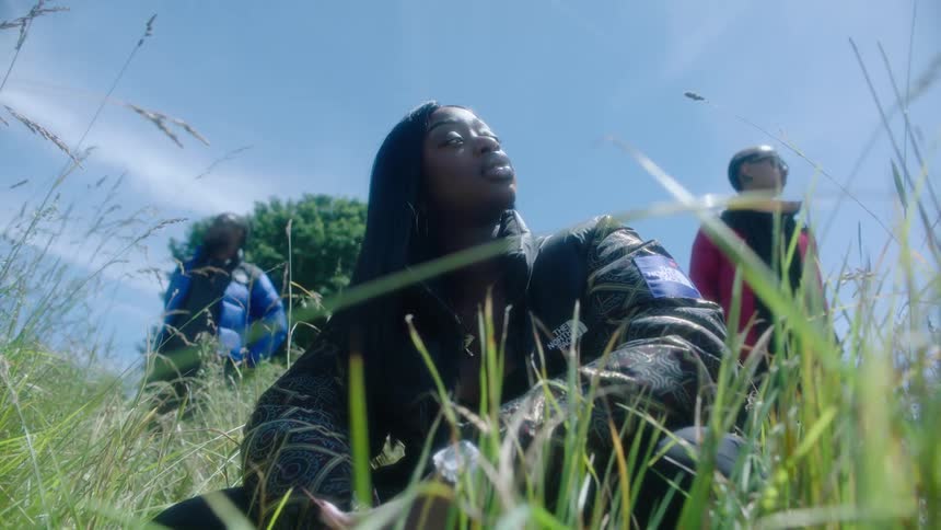 Young woman wearing a thick jacket sitting on the grass in front of two men looking at the horizon