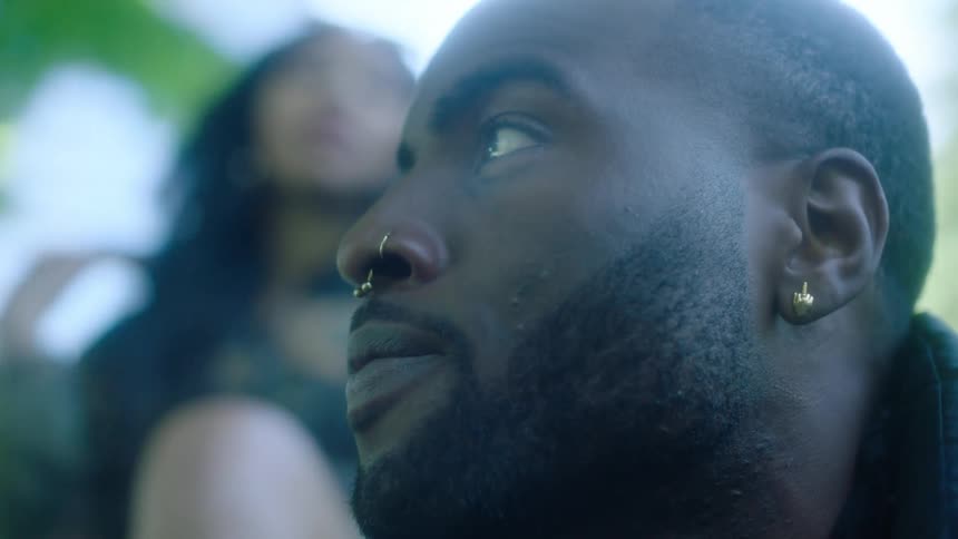 Close up of the face of a young attractive man with a woman standing behind him looking at the camera