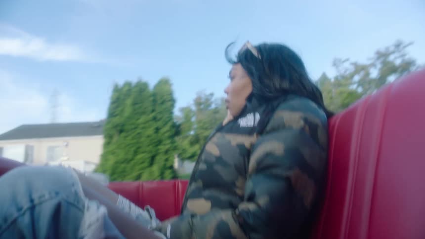 Woman rides in convertible with the top down as it drives past large homes