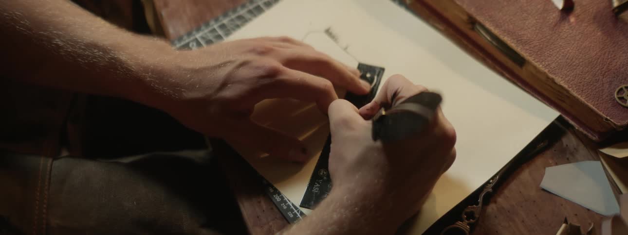 A man is sitting at a table drawing on paper with a ruler