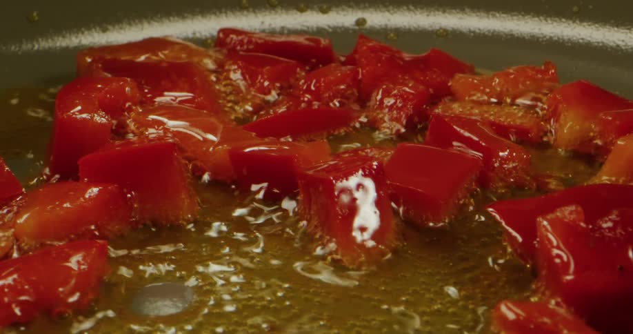 Close up of bright chopped red peppers frying on oil inside a pan