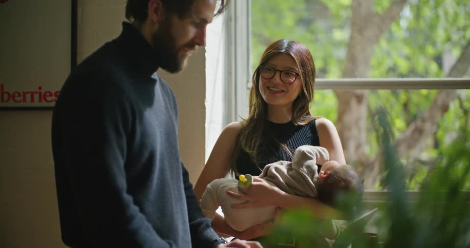 A man uses a laptop while talking to a woman cradling a baby next to him