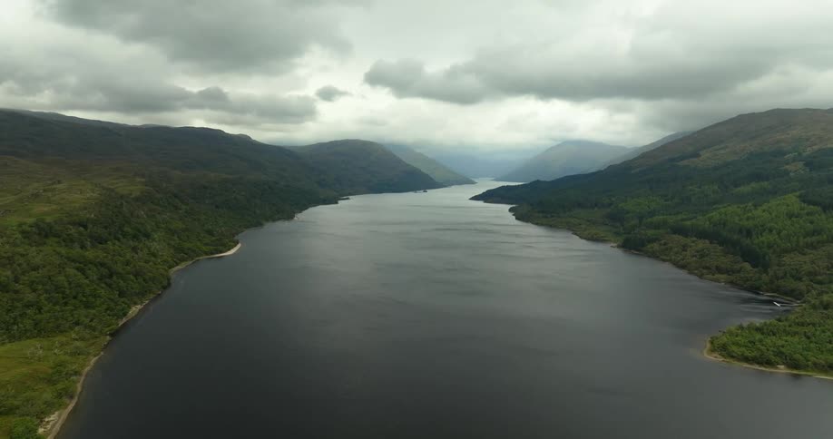Forested mountains border river stretching to misty horizon under an overcast sky