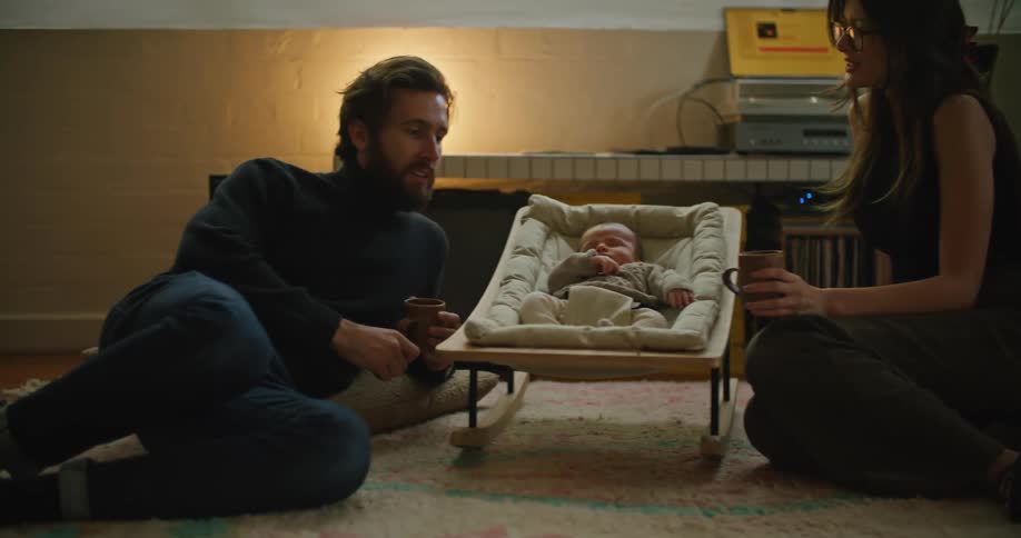 Young couple laying on the carpet in the living room talks while watching the baby