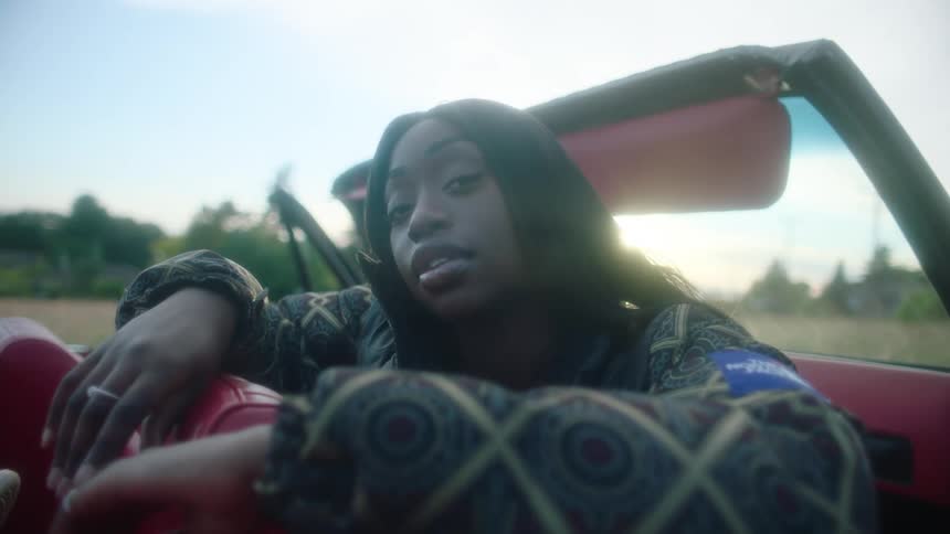 A woman sitting in a convertible faces backward in her seat to look into the camera
