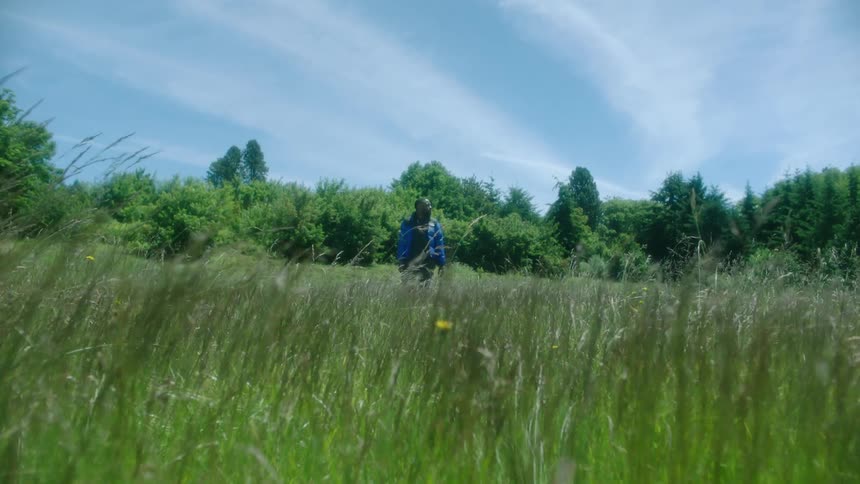 Man in blue coat looks around in green field on windy day