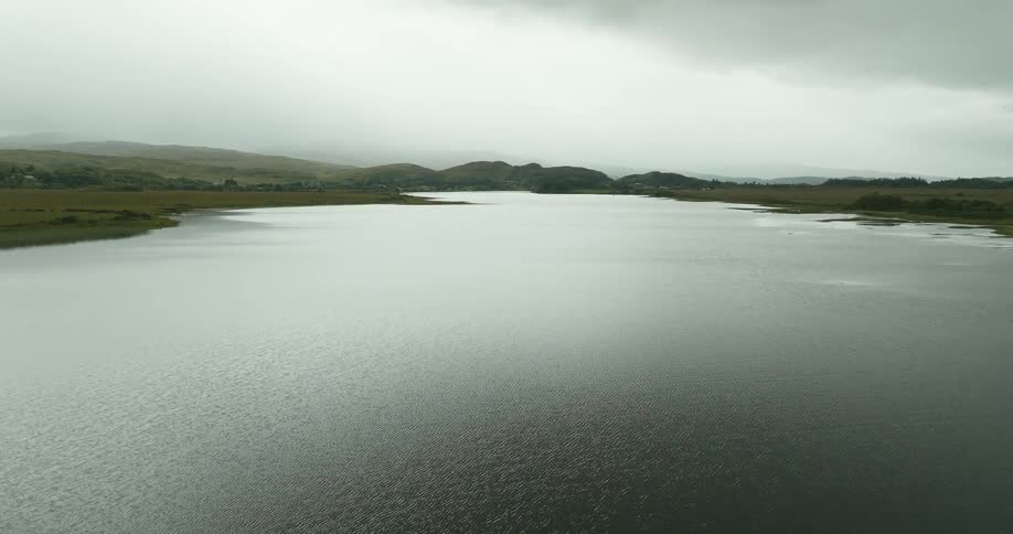 Silvery water stretches between green shores and hills under an overcast sky