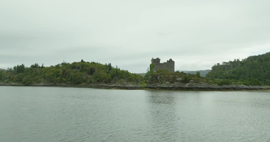 An old castle sits along the coast with nearby forests and mountains in the distance