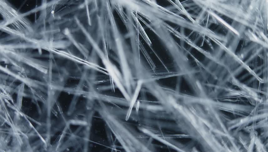 Twisting close up of thing ice crystals forming in front of a black background