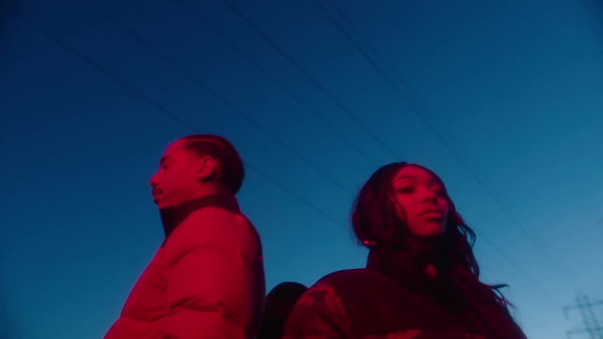 Under red lighting four people stand back to back at night under powerlines