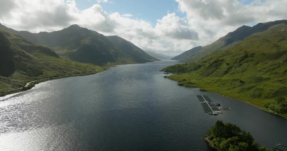 A loch running through a mountain valley during the day with a fish farm