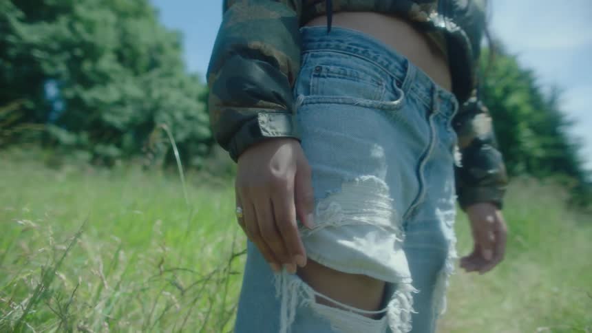 Close up of a model wearing damaged distressed jeans on a grass field at daytime