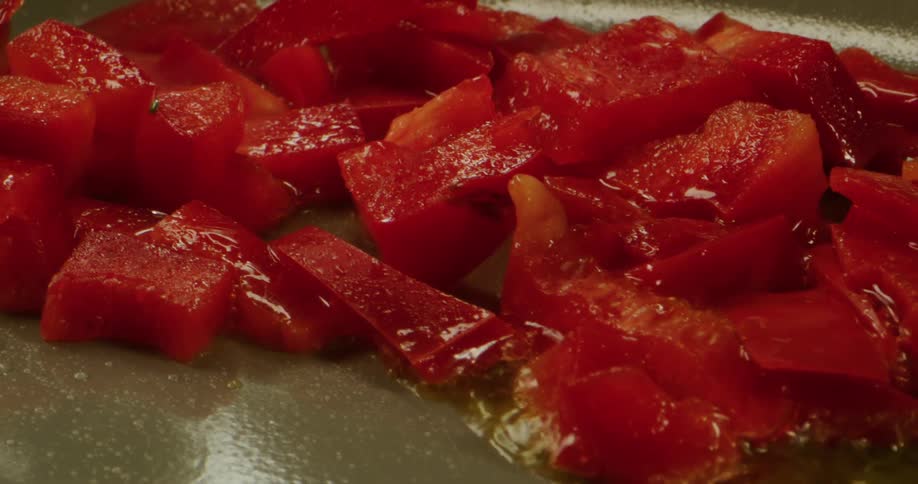 Close up of red sliced peppers being fried in frying pan