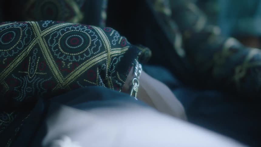 Close up of a metallic bracelet on the wrist of a person sitting on a dimly lit room