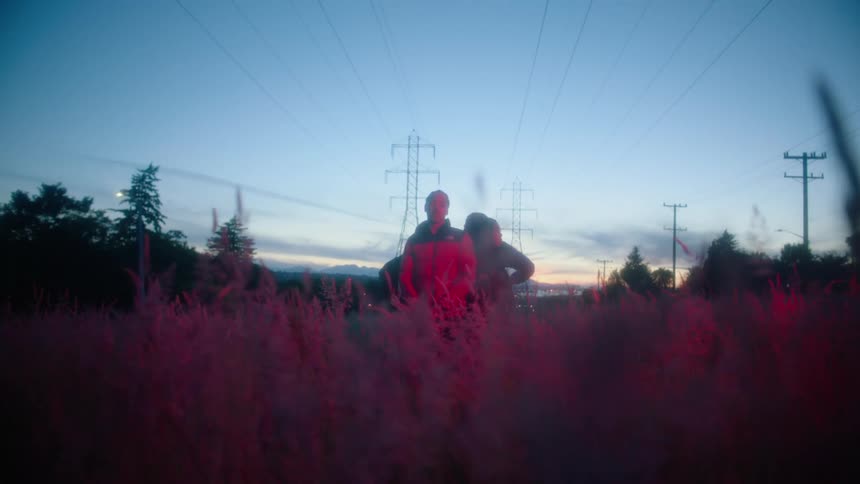 Two people stand in tall weeds tinted pink