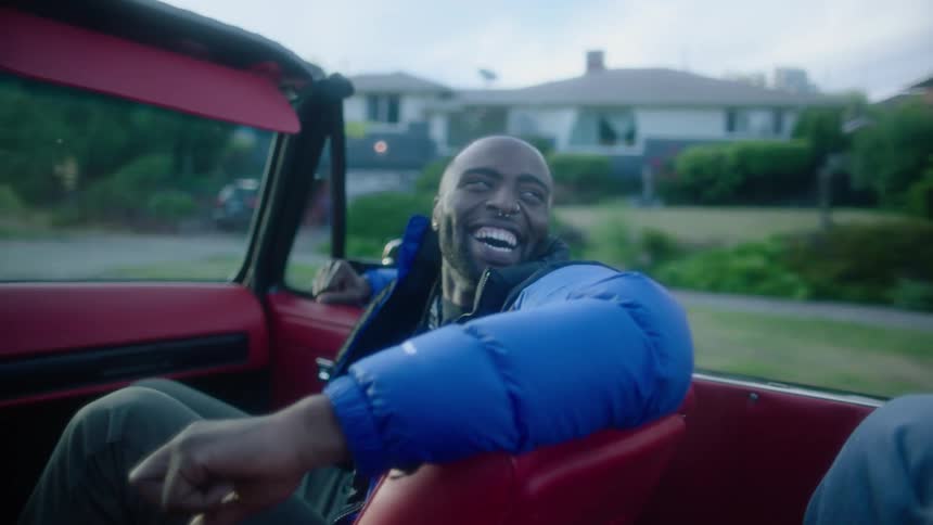 Happy young man wearing a jacket laughs while sitting on the passenger seat of a car driving in the neighborhood