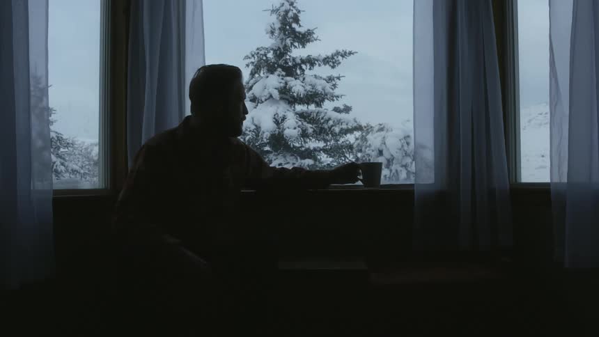 A man sits and drinks from a mug at home