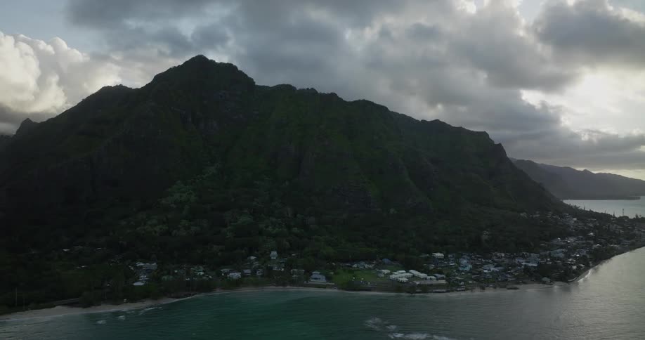 Town hugs coast at the base of forested mountains under an overcast sky