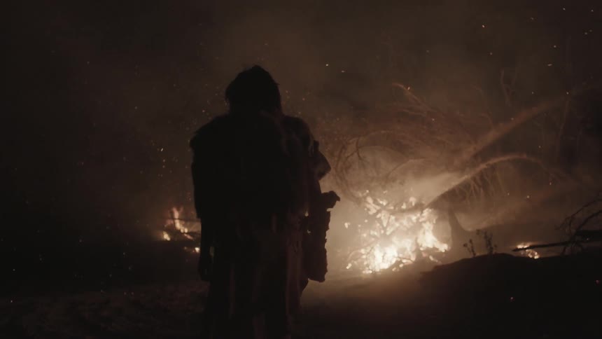 A man watching a pile of branches burning at night