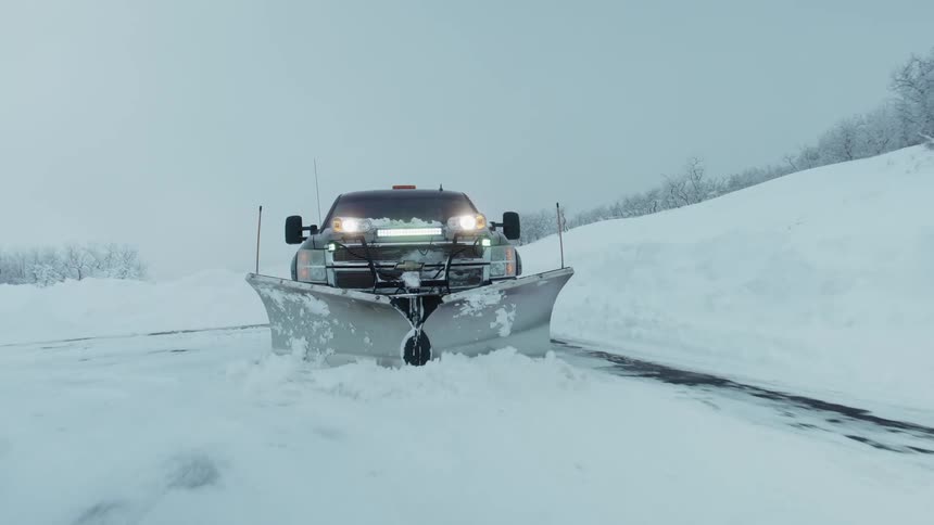 Government vehicle with flashing light and an attached plow clears snow off the road during a snowstorm