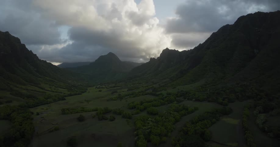 An aerial view of a valley in the hills with large clouds overhead