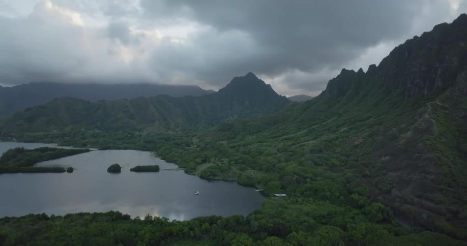 Aerial view of building in forest next to lake and mountain range on cloudy day