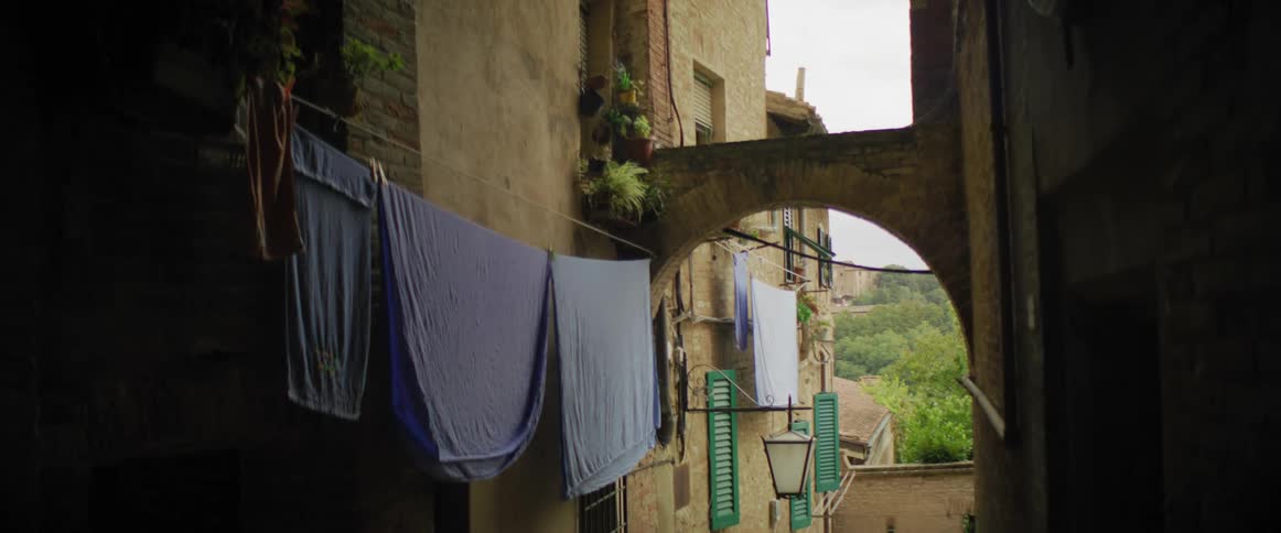 Bedsheets are hung out to dry on a laundry line in an alley between apartment buildings