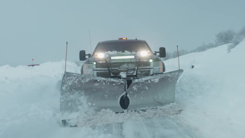 A snow plow drives down a road and plows snow off