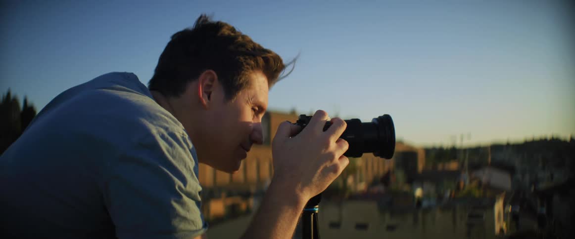 Male photographer with blue t shirt takes photograph with camera on tripod in historical site