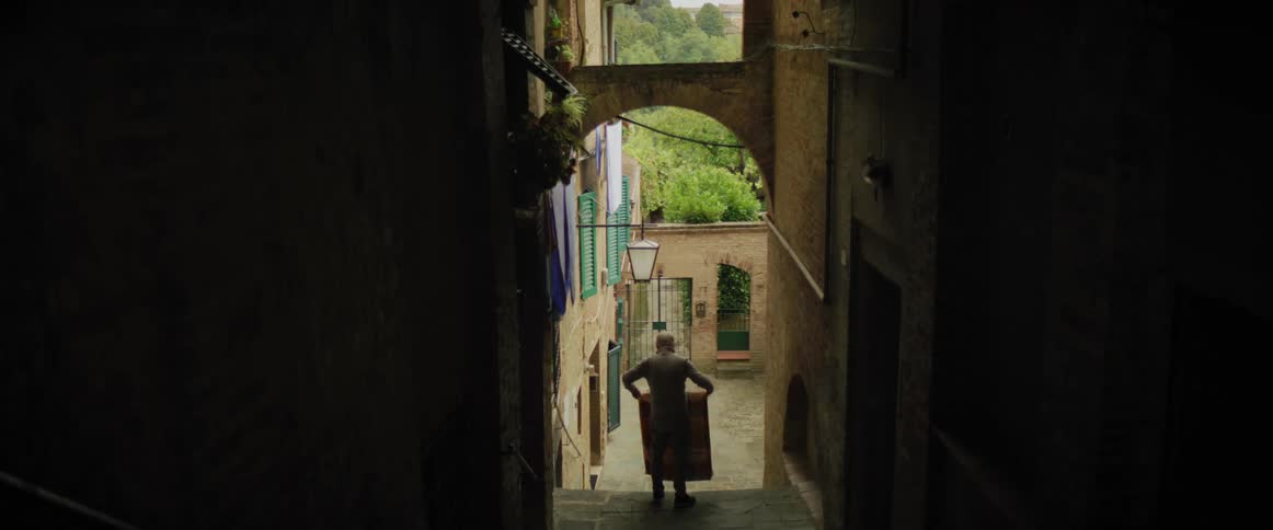 A man standing on the steps above a courtyard shakes out and folds a blanket