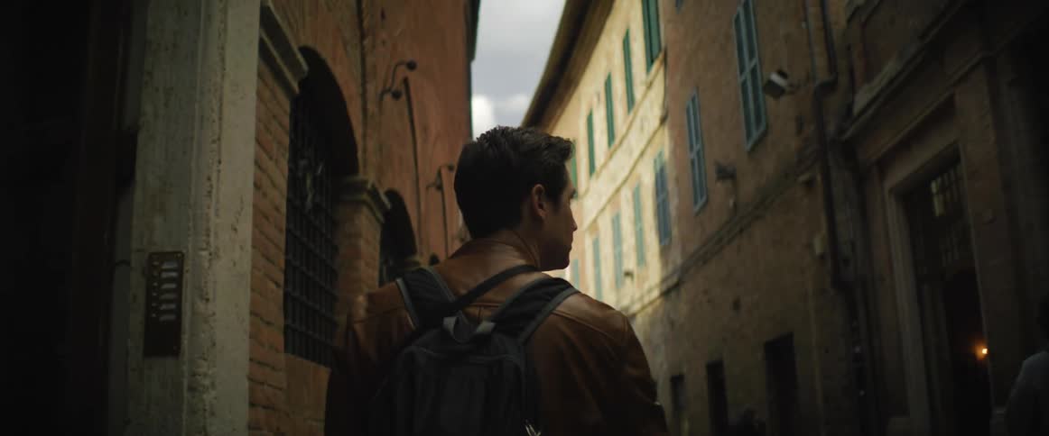 Man with brown shirt and backpack walks down the alley