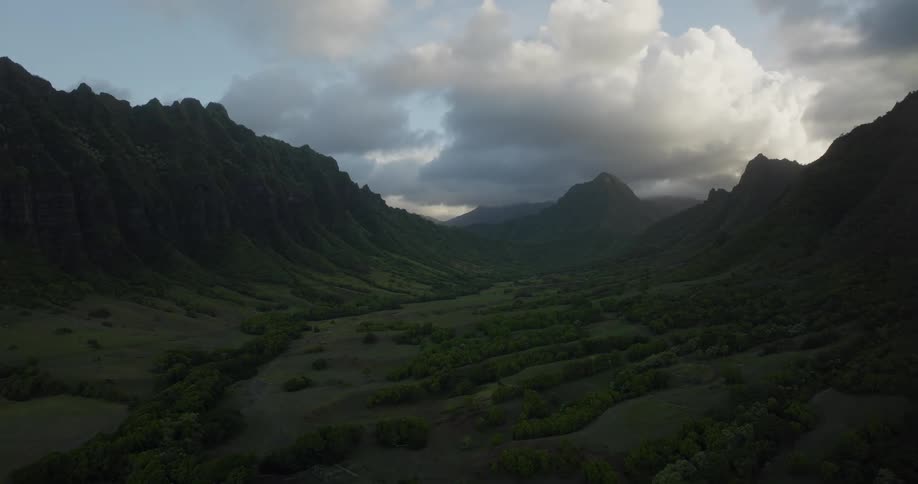 Tall and rocky mountains rise high above a valley full of grass and trees