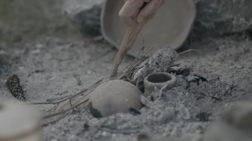 A pan pokes sticks in an ashy pile