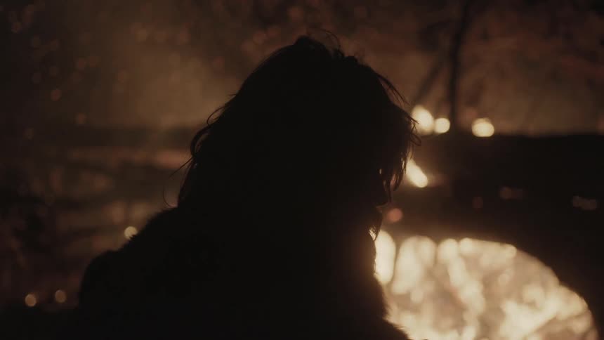 A person sits beside a large burning bonfire
