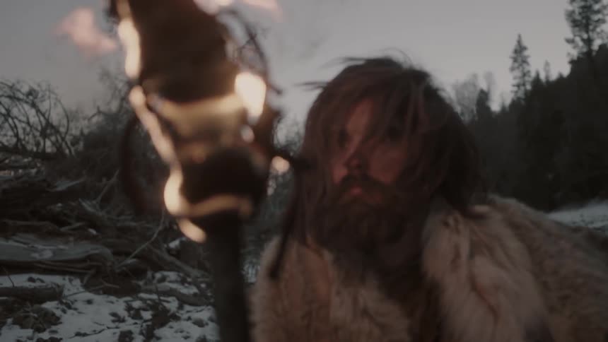 A man wearing fur brings a lit torch near his face